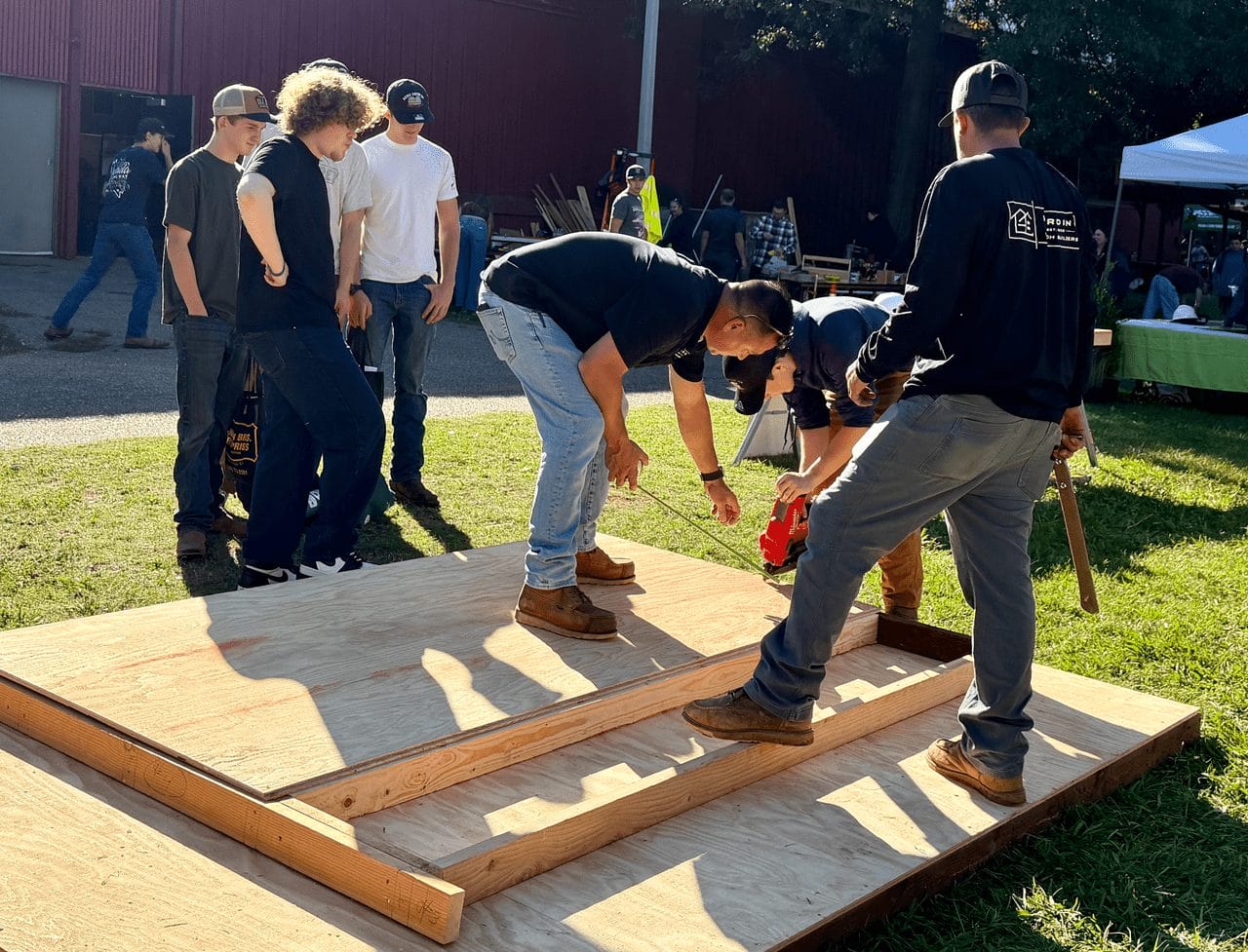 Crew member guiding students as they assemble a timber wall frame outdoors