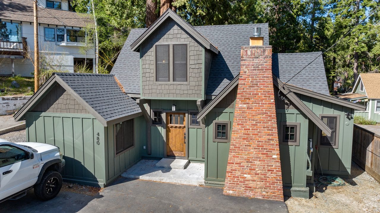 Green craftsman-style home with a stone chimney and multiple gables