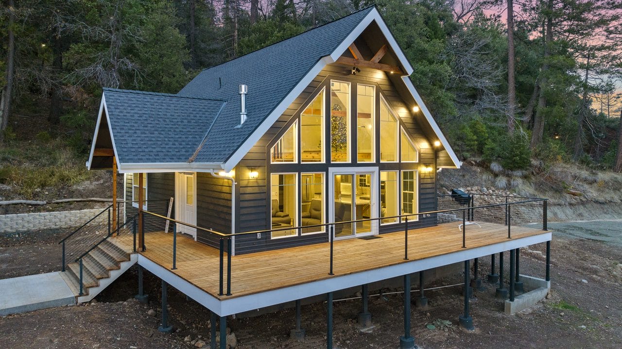Shed-roof cabin with a glass gable end glowing at dusk above an elevated deck