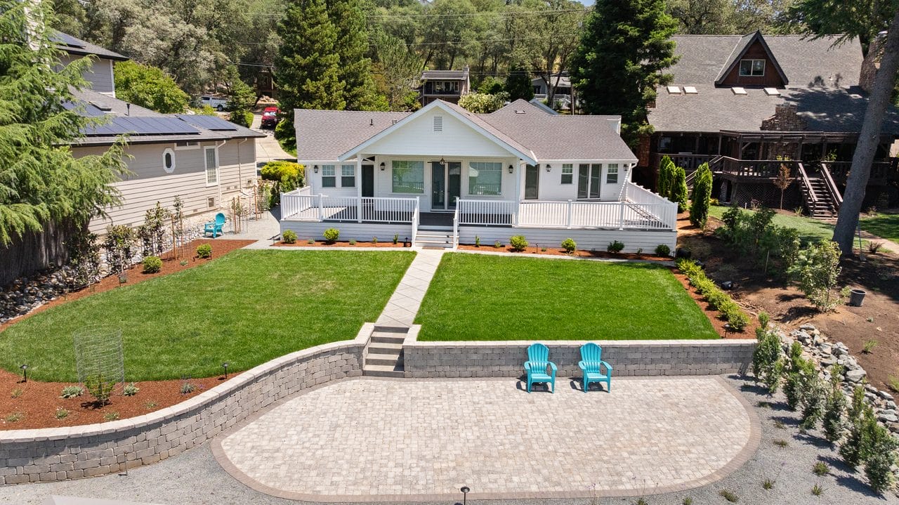 Aerial view of a white ranch home with lawn, gravel turnaround and patio chairs