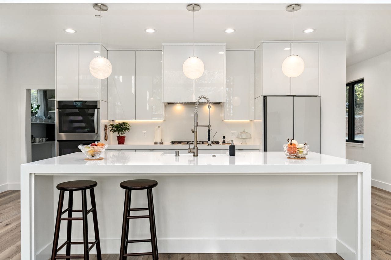 Modern white kitchen with waterfall island, bar stools and globe pendant lights
