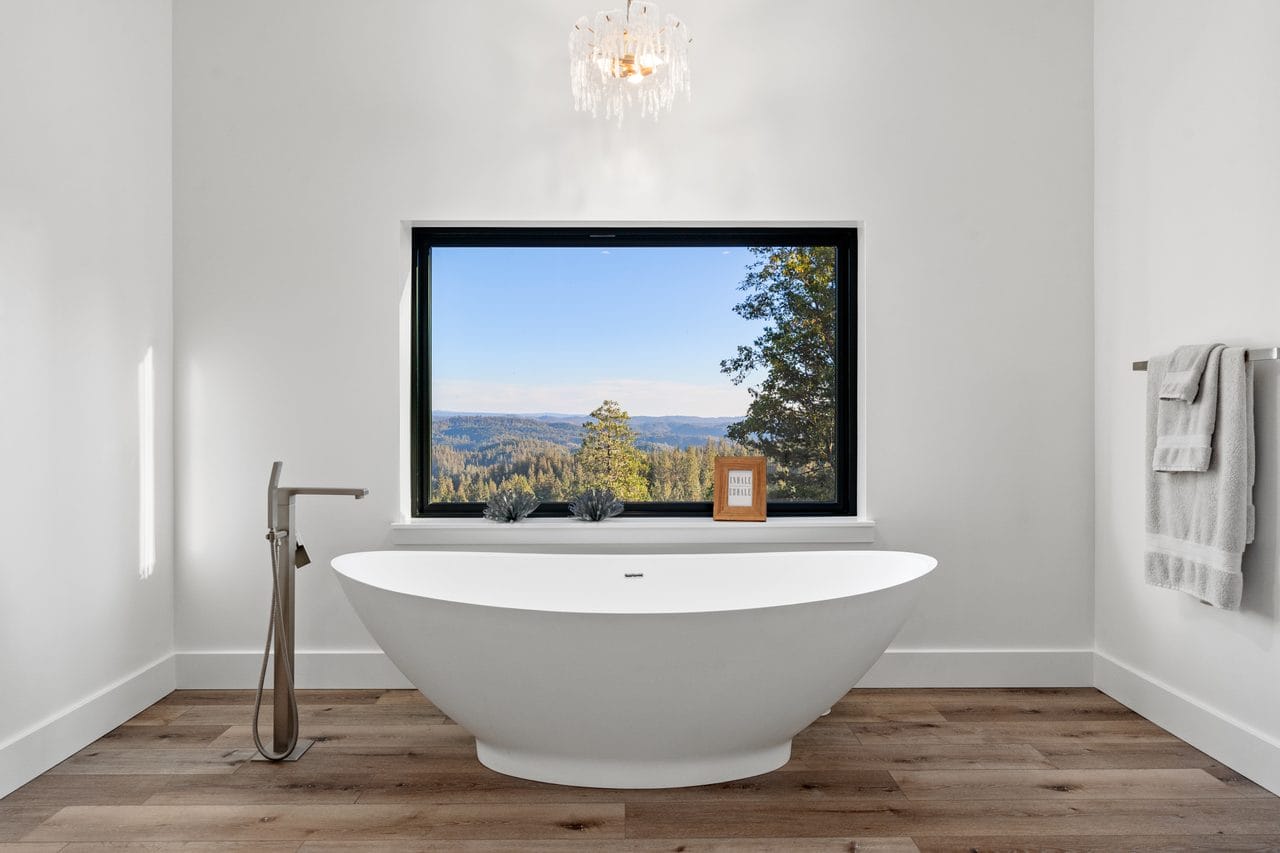 Freestanding soaking tub with floor-mounted filler beneath a picture window