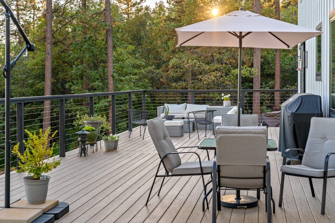 Deck with umbrella dining table and chairs surrounded by tall pines