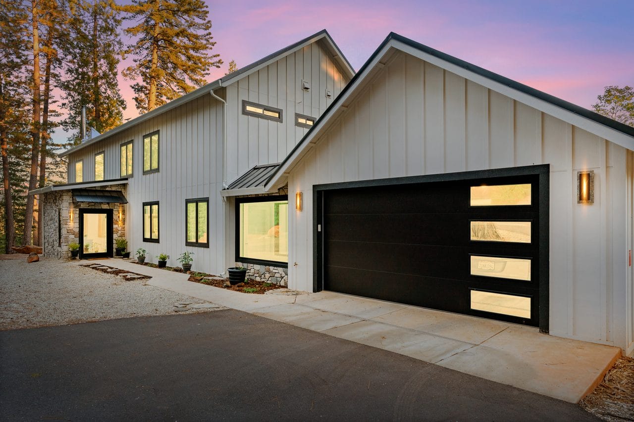 Modern farmhouse lit at dusk with black garage door and warm wood accents