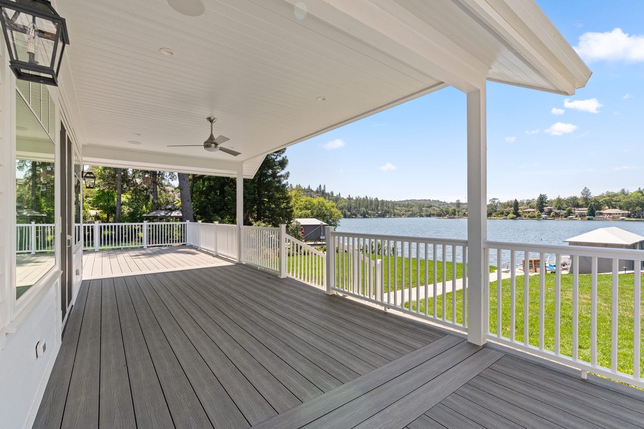Covered porch with composite decking and white railing overlooking a lake