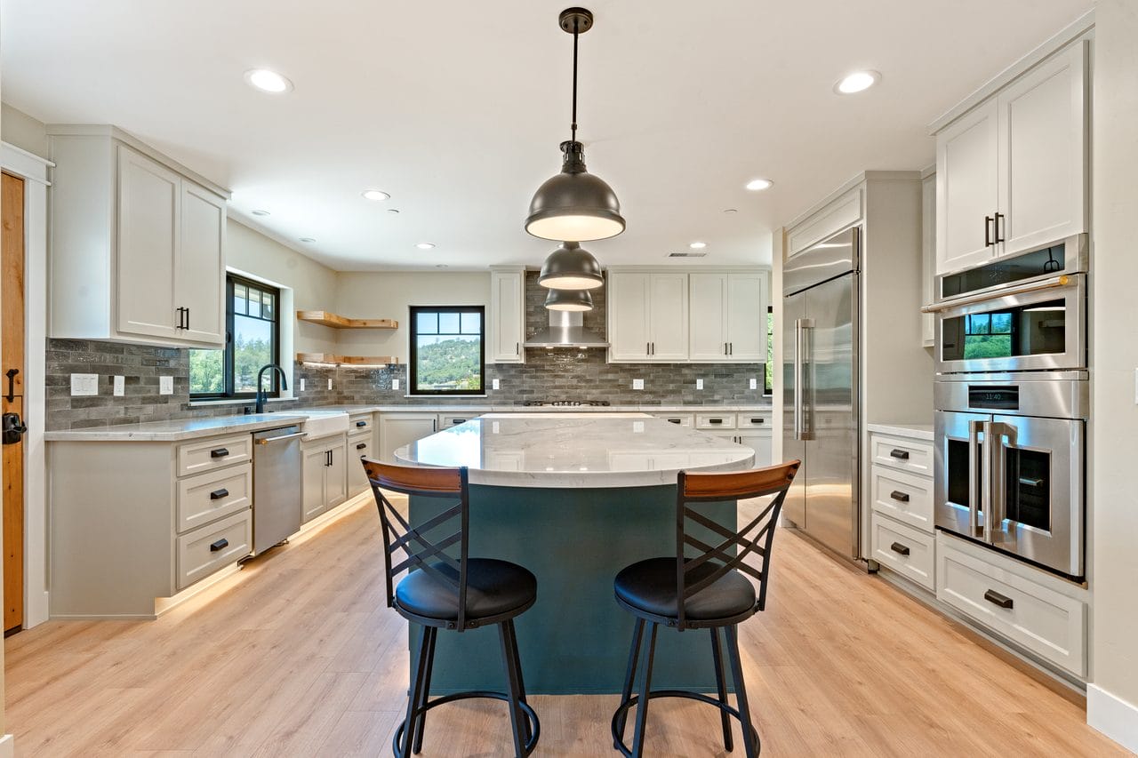 White kitchen with grey island, pendant light, wall ovens and bar seating