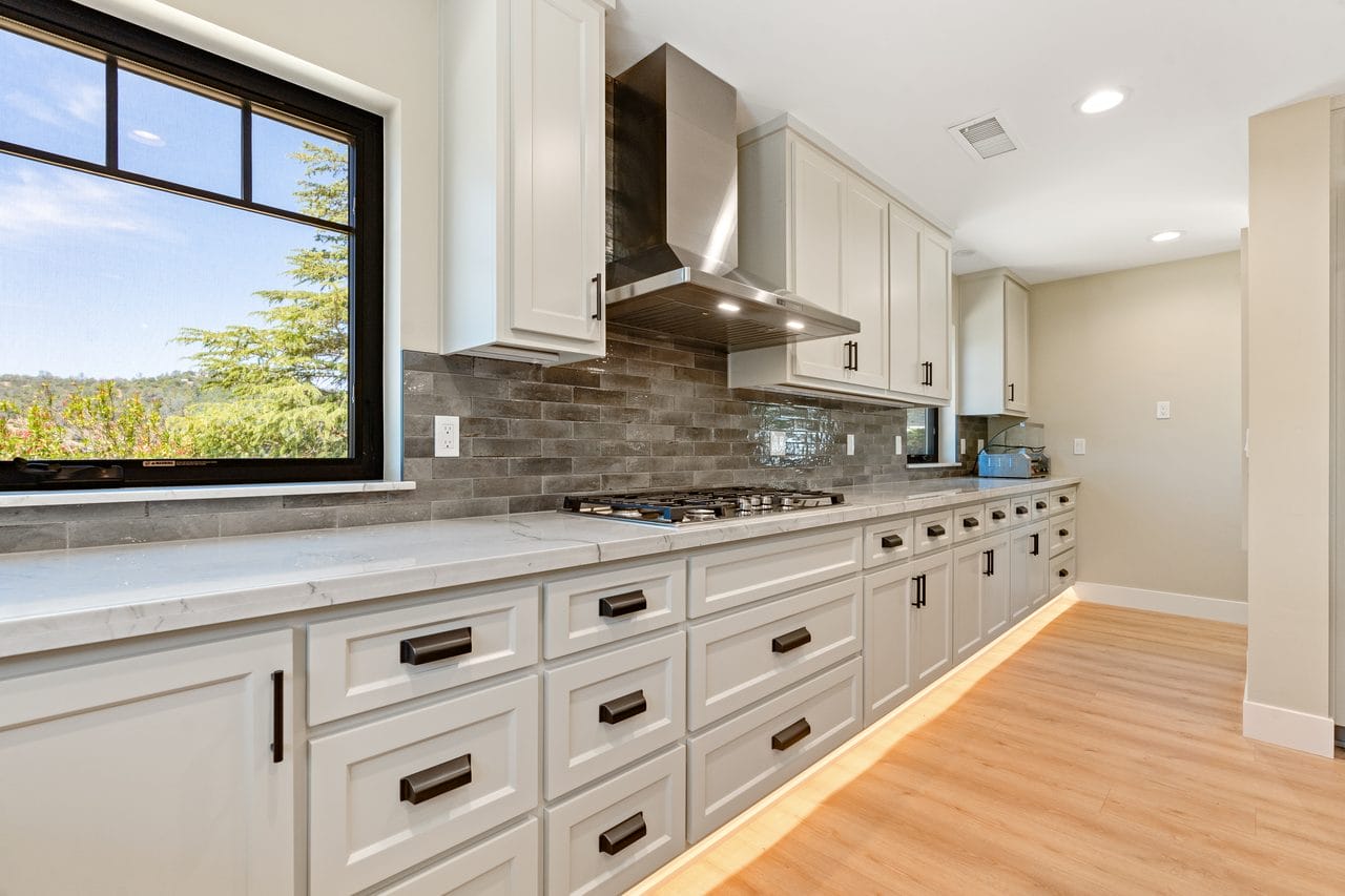 White kitchen with a long cabinet run, stainless hood and brick backsplash