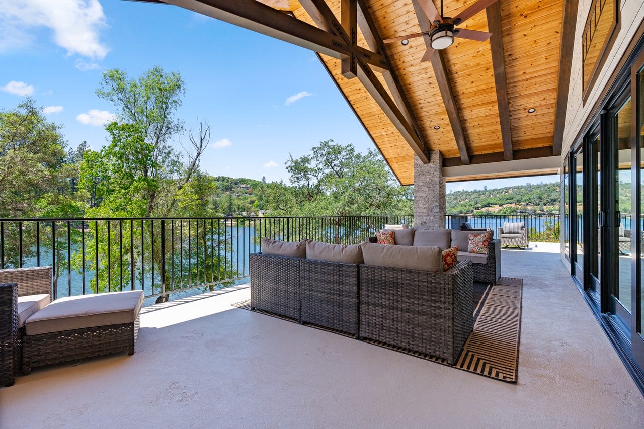 Covered deck with timber ceiling and wicker seating overlooking treetops and lake