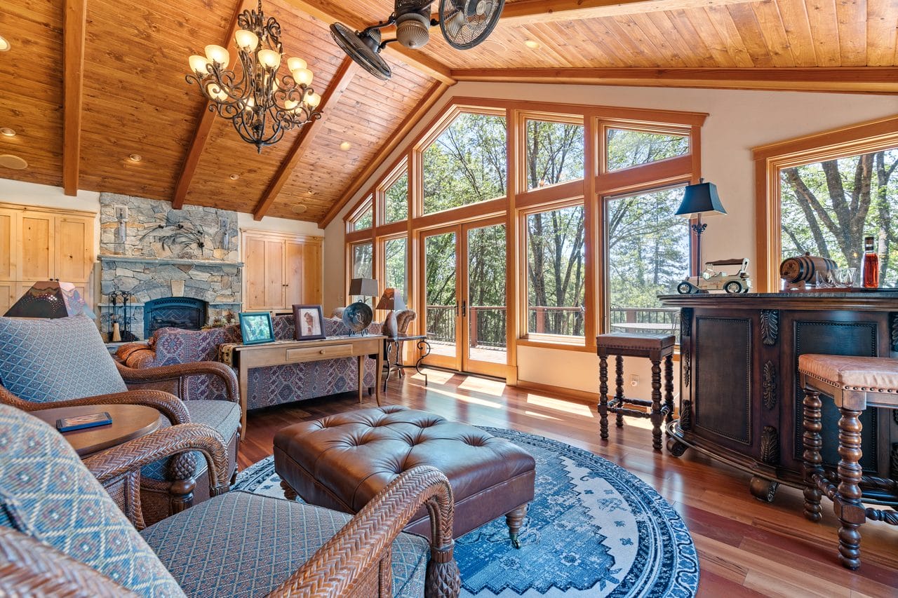 Living room with vaulted pine ceiling, stone fireplace and wall of windows