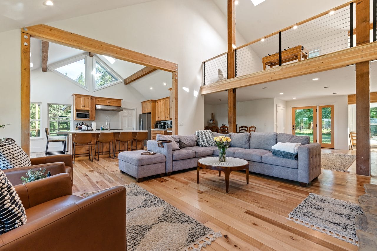 Great room with exposed timber trusses, open kitchen and loft overlook