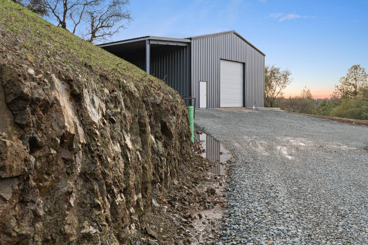 Gravel drive cut into a hillside leading to a steel shop building at sunset